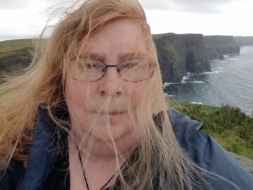 Picture of Xap Esler at a windy coast; the hair is blown in her face.
