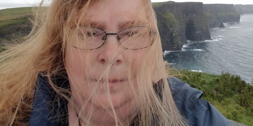 Picture of Xap Esler at a windy coast; the hair is blown in her face.